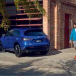 ZR-V azul estacionado junto a um edifício, enquanto um homem caminha no passeio e segura uma raquete, em ambiente urbano e iluminado pela luz natural.