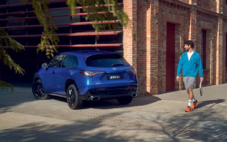 ZR-V azul estacionado junto a um edifício, enquanto um homem caminha no passeio e segura uma raquete, em ambiente urbano e iluminado pela luz natural.