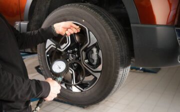 Mecânico a verificar a pressão de um pneu automóvel durante a revisão do carro numa oficina, utilizando um manómetro.