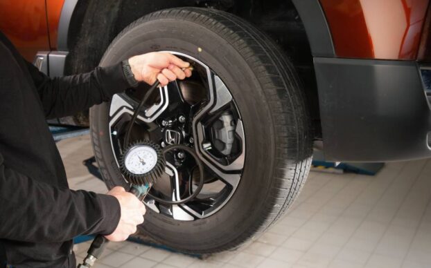 Mecânico a verificar a pressão de um pneu automóvel durante a revisão do carro numa oficina, utilizando um manómetro.