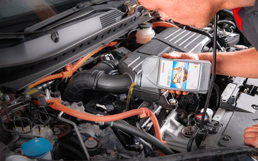 Técnico a adicionar óleo de motor durante a revisão do carro no compartimento do motor automóvel.