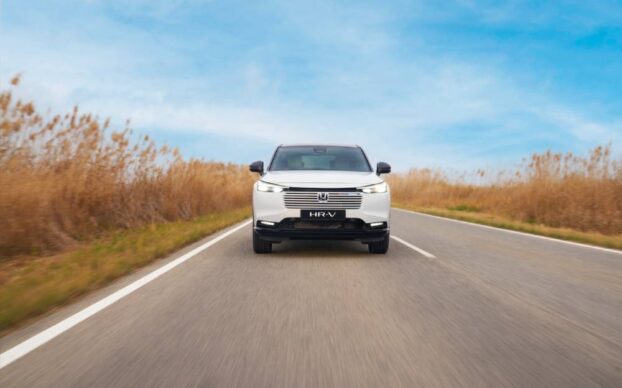 Vista frontal do Honda HR-V híbrido a circular numa estrada, com paisagem aberta, destacando o seu design moderno.