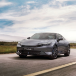 Honda Prelude 2026, na cor Meteoroid Grey Metallic, a circular em estrada aberta com uma paisagem natural, destacando o seu design moderno.