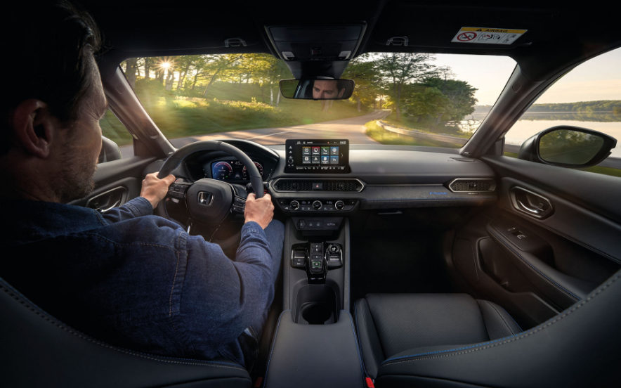 Interior do Honda Prelude 2026 com condutor ao volante, painel digital e botão S+Shift visível, com vista da estrada ao pôr do sol. 