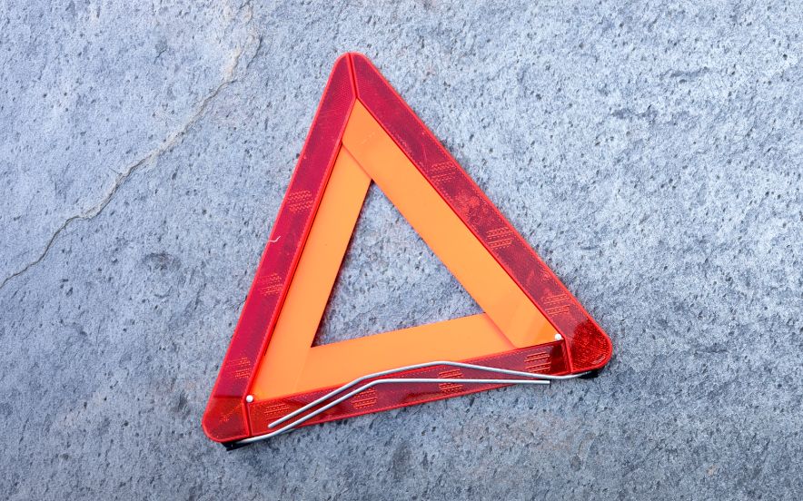 Triângulo vermelho de aviso a sinalizar pneu furado do veículo numa estrada escura