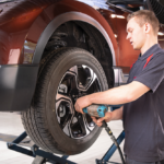 Técnico a substituir um pneu numa viatura elevada numa oficina Honda, utilizando uma ferramenta elétrica para apertar a roda.
