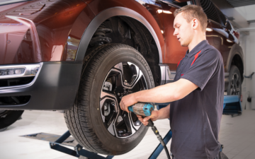 Técnico a substituir um pneu numa viatura elevada numa oficina Honda, utilizando uma ferramenta elétrica para apertar a roda.