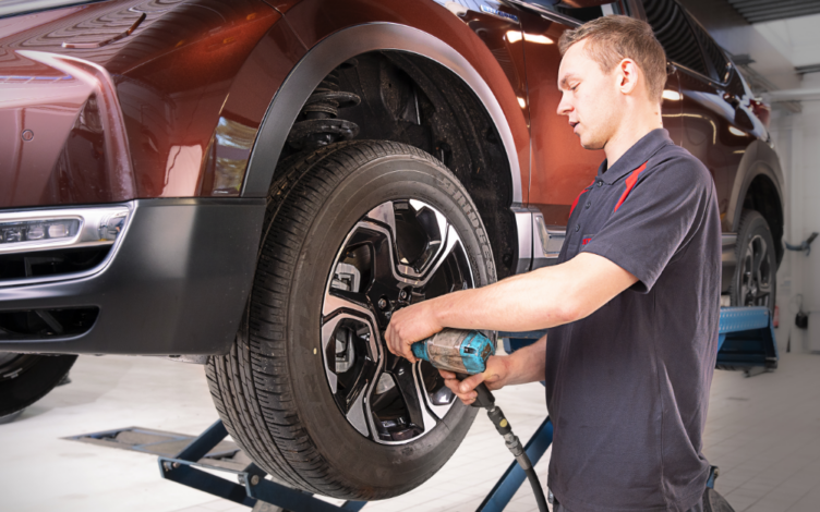 Técnico a substituir um pneu numa viatura elevada numa oficina Honda, utilizando uma ferramenta elétrica para apertar a roda.