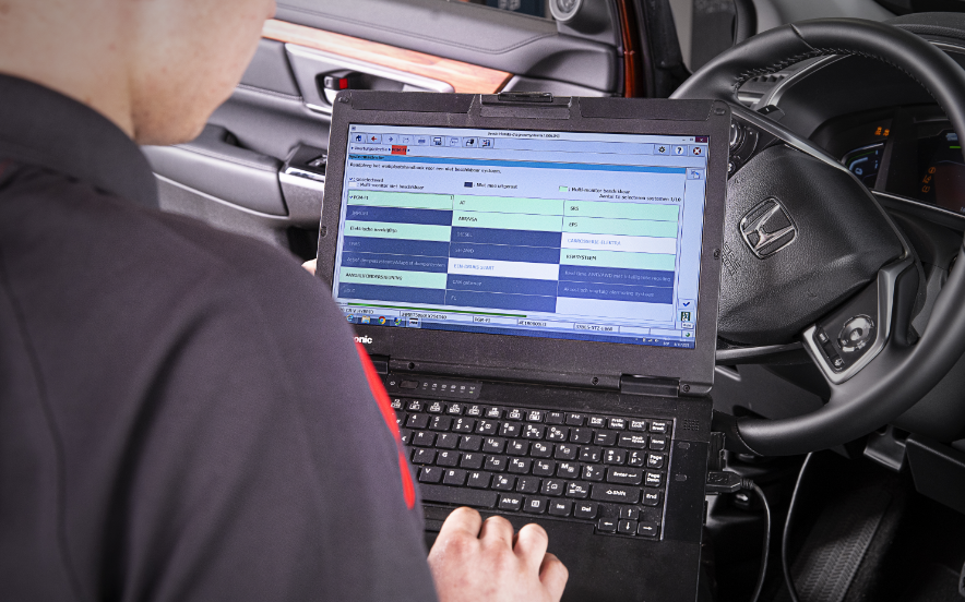 Técnico a realizar um check-up automóvel numa viatura Honda, verificando componentes como pneus e motor numa oficina autorizada.