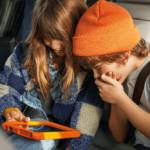 Crianças no interior de um Honda a brincar com um tablet a caminho das férias desportivas