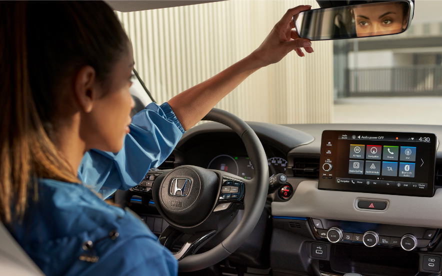 Interior do Honda HR-V com condutora a ajustar o espelho retrovisor, com o painel digital visível.